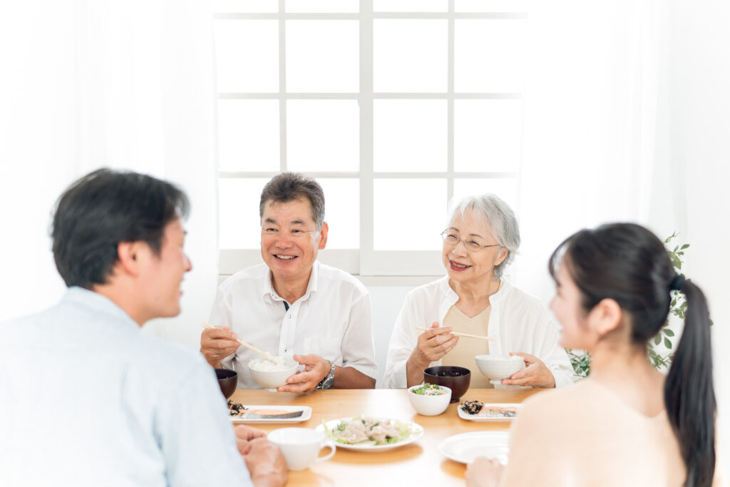 日本人の高齢夫婦と一緒に、若い夫婦が楽しそうに食事をしている。テーブルには和食が並んでいる